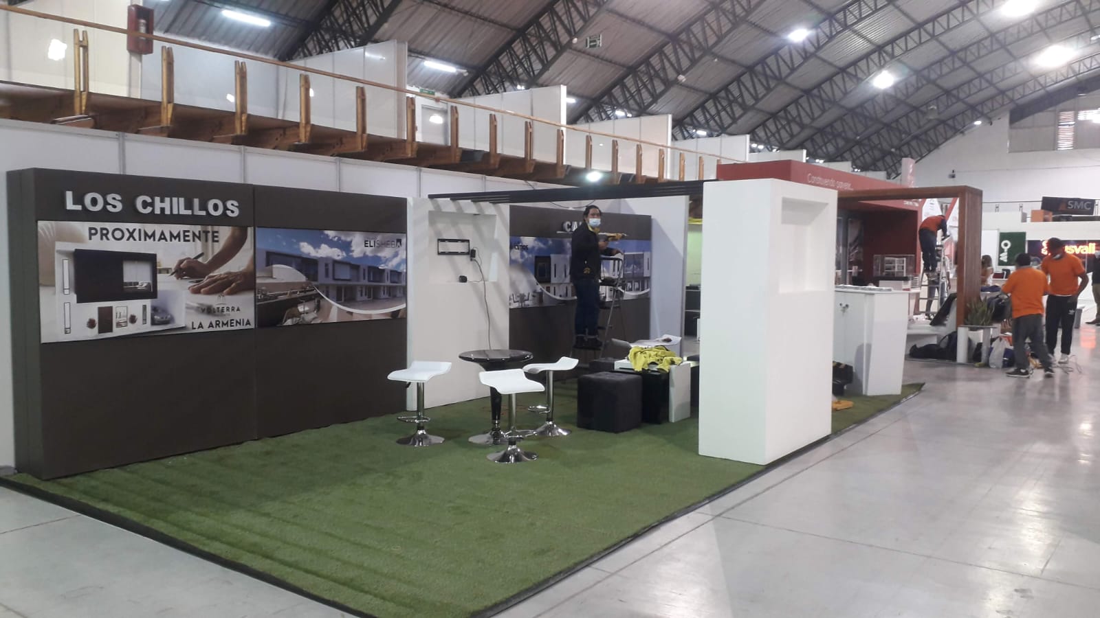 Stand inmobiliario Los Chillos en una feria, con paneles gráficos y piso de césped sintético