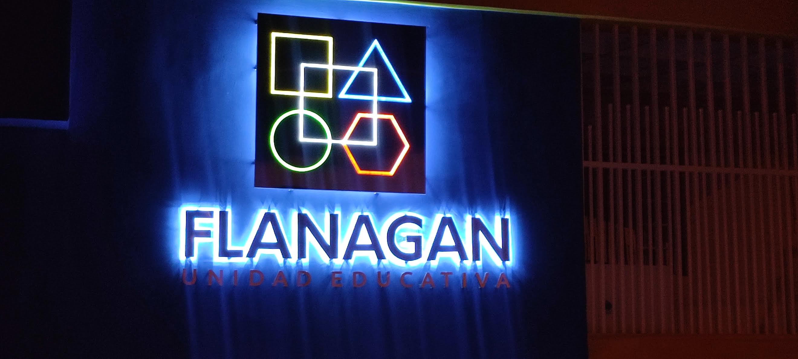 Fachada de la Unidad Educativa Flanagan de noche con logo de figuras en neón y letras con luz azul
