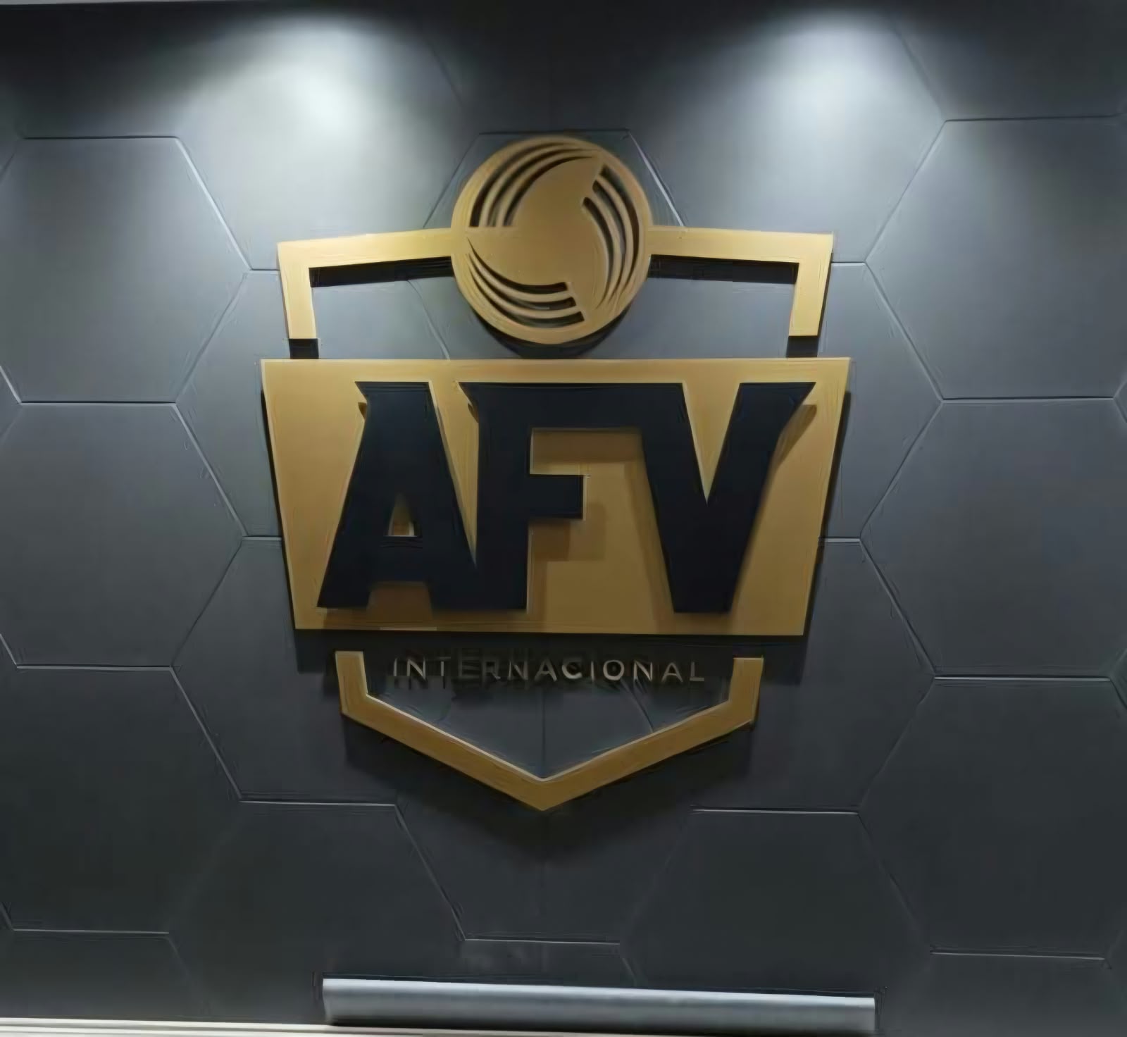 Escudo dorado de AFV Internacional en relieve sobre una pared gris