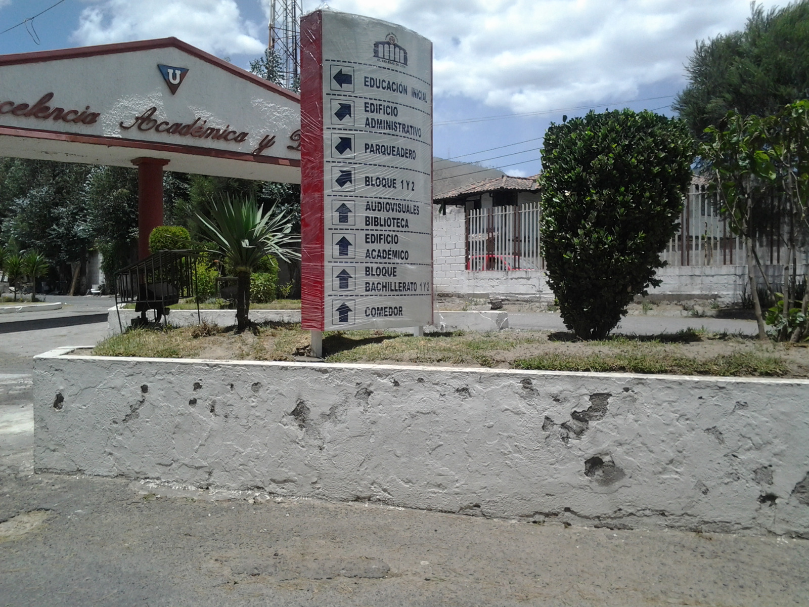 Tótem direccional con flechas a los edificios en la entrada de un colegio