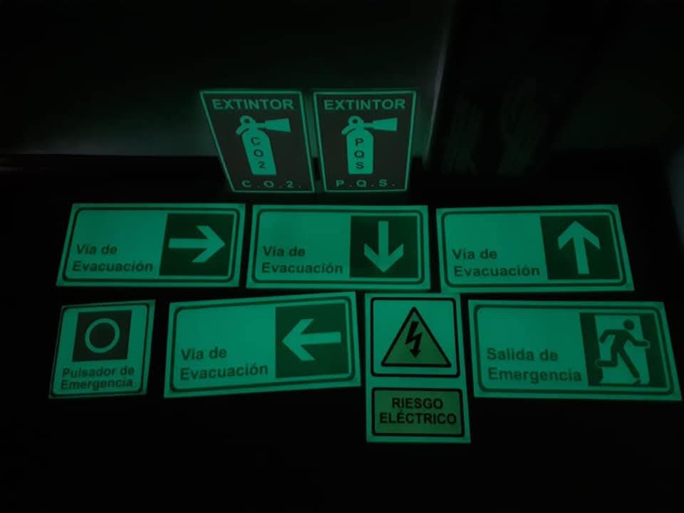 Señales fotoluminiscentes de extintor, vía de evacuación, riesgo eléctrico y salida de emergencia brillando en la oscuridad
